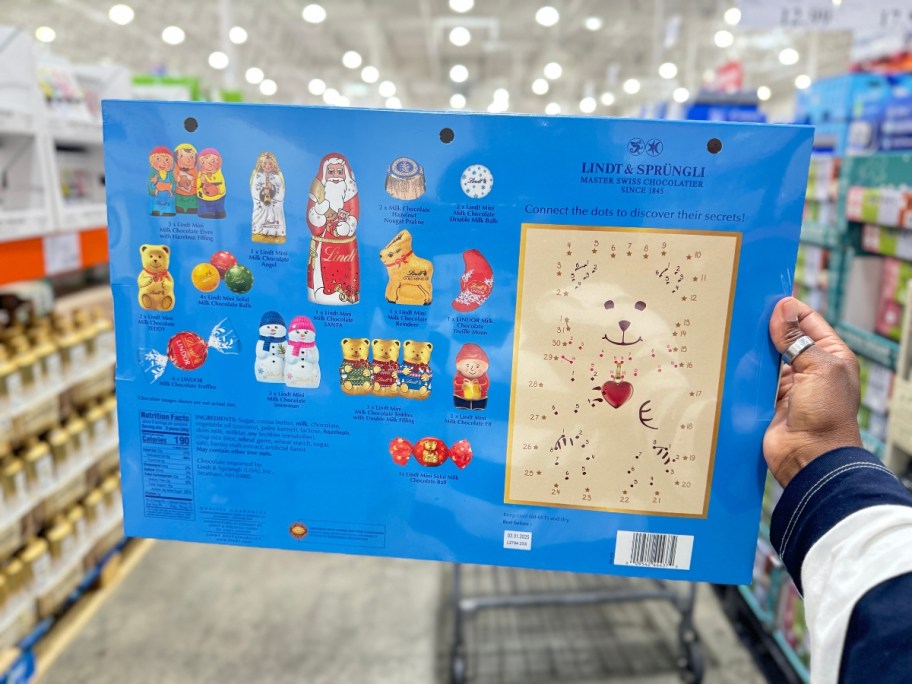 hand holding a colorful Lindt Chocolate Advent Calendar box showing the back of it with the candy included