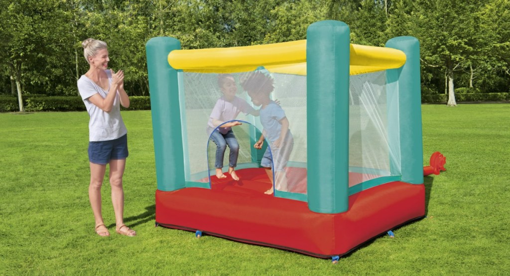 mom clapping as kids play inside of large bouncer that's displayed on the grass