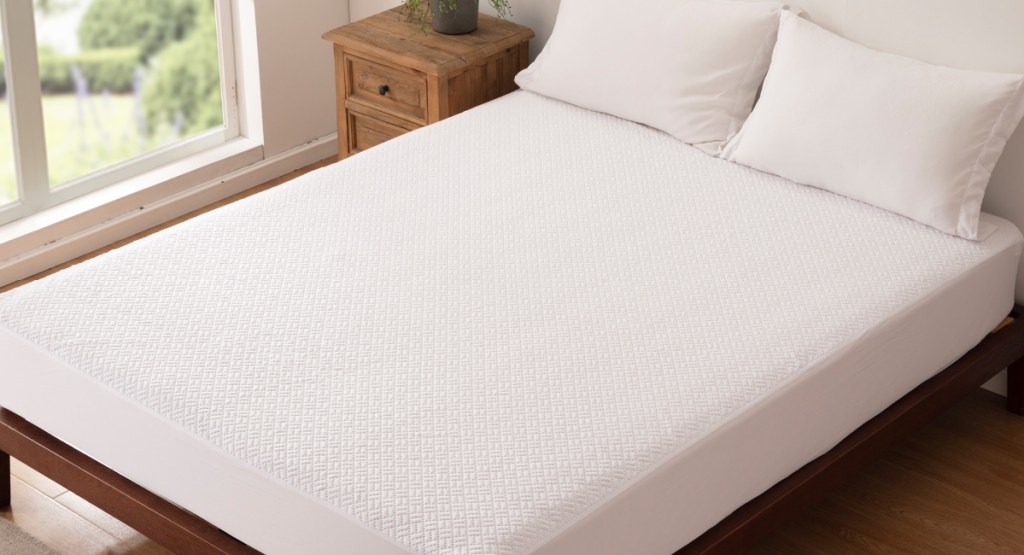 white mattress protector with pillows on the bed and next to the nightstand