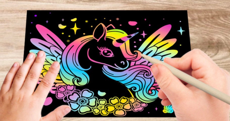 hands drawing unicorn on scratch art paper