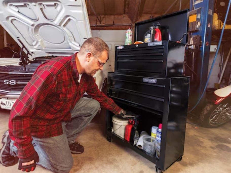 man putting tools in a 4 foot tall black Craftsman tool cabinet next to a car with the hood up