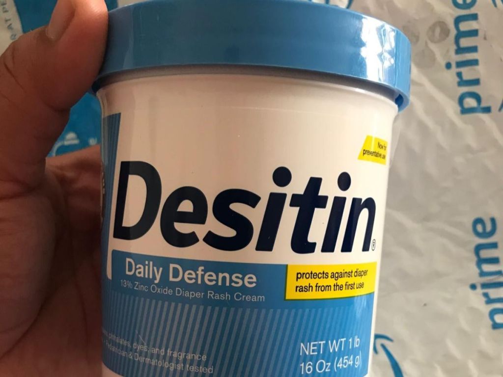 A hand holding a tub of Desitin