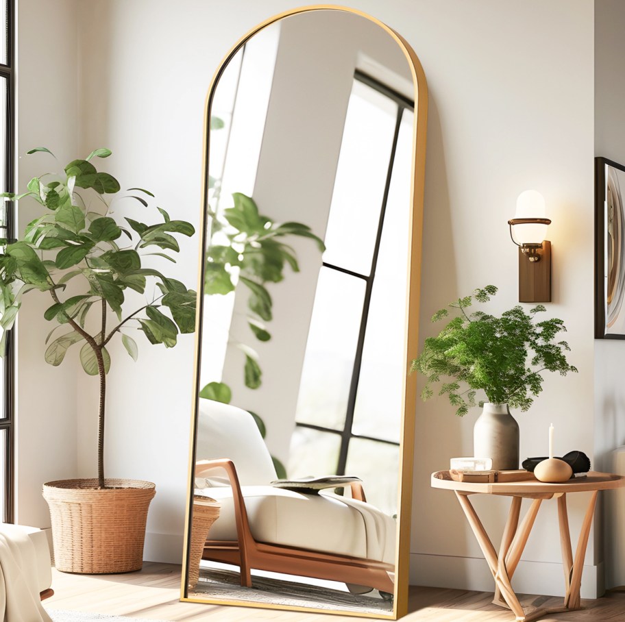 gold full length arched mirror leaning against wall