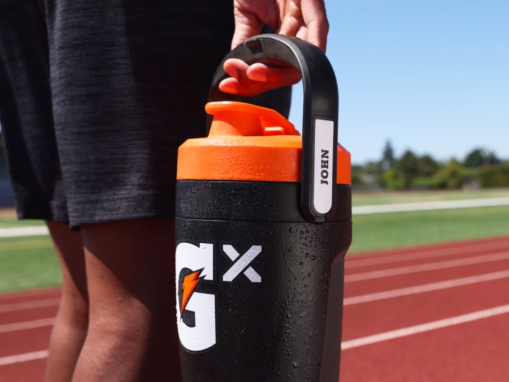 person holding a black gatorade jug that says john on the handle