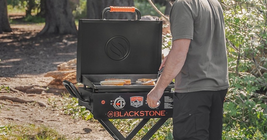 man grilling food on a 2 burner Blackstone gridle that has a hood