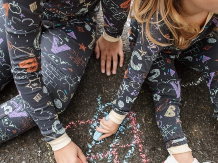 kids wearing black long sleeve pj's with sidewalk chalk print, playing with sidewalk chalk on black asphalt 