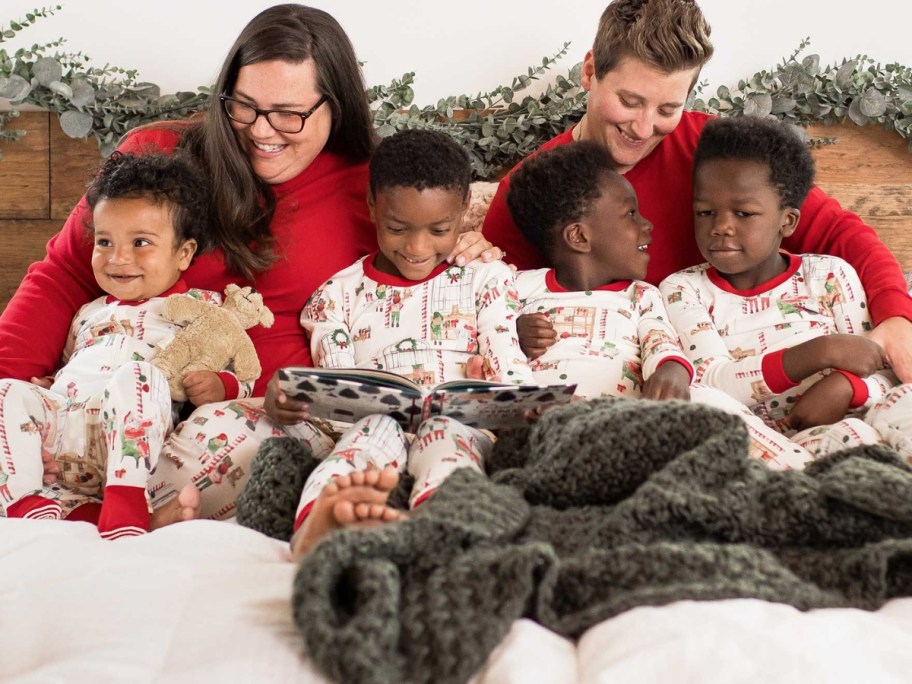 family with parents and kids sitting in bed wearing matching Christmas pajamas