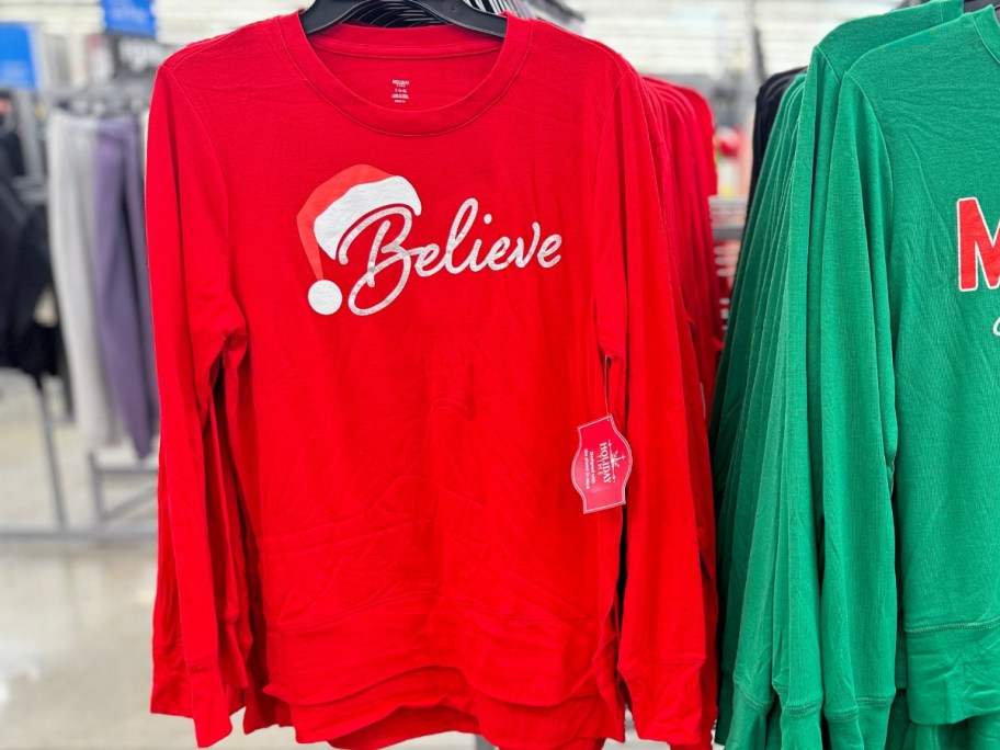 women's red Christmas sweater with "Believe" and a Santa hat on a store rack