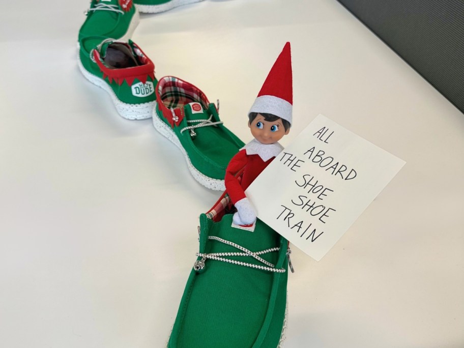 green and red HEYDUDE Holiday Elf style shoes with an Elf on the Shelf in one of them