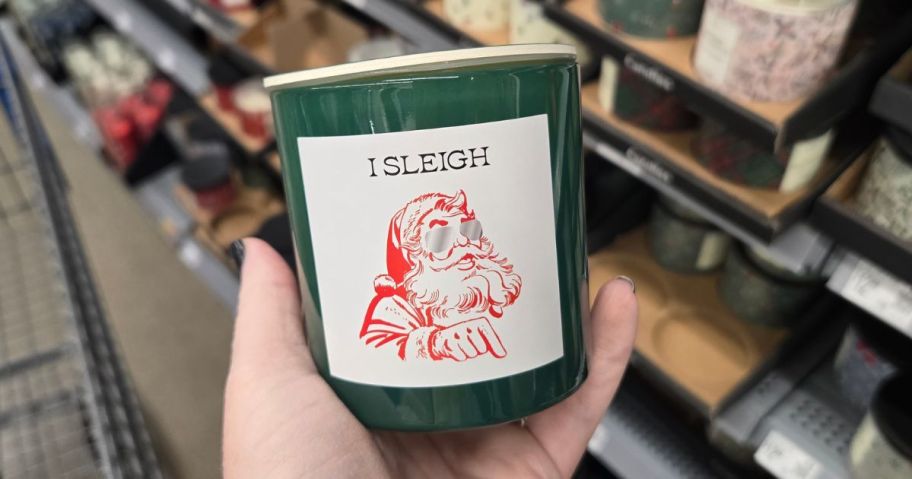 hand holding Mainstays "I Sleigh" Dirty Santa Scented Candle 6oz in store