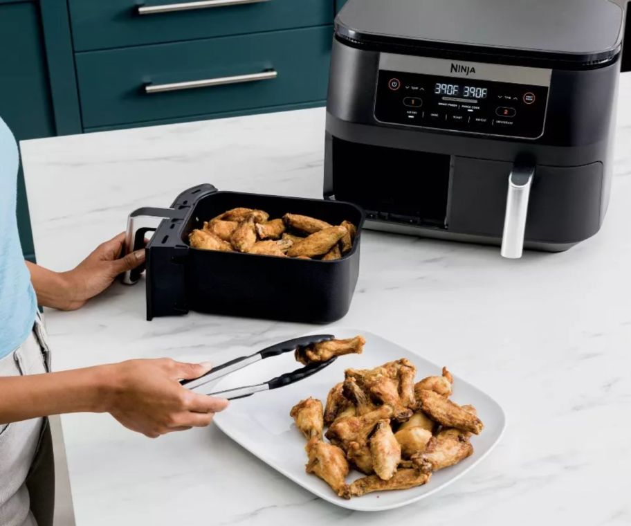 a woman taking chicken wings out of an air frey basket