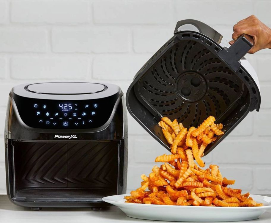 a persons hand showi dumping fried out of the basket of a PowerXL Vortex Pro 8-quart Air Fryer on to a plate