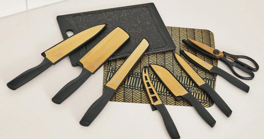 a set of black and gold knives, kitchen sheers, cutting board and cutting mats on a counter