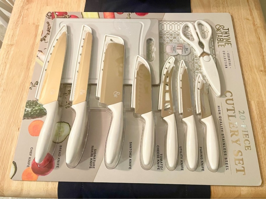 a set of cream and gold knives, kitchen sheers, cutting board, and cutting mats in the packaging on a kitchen table