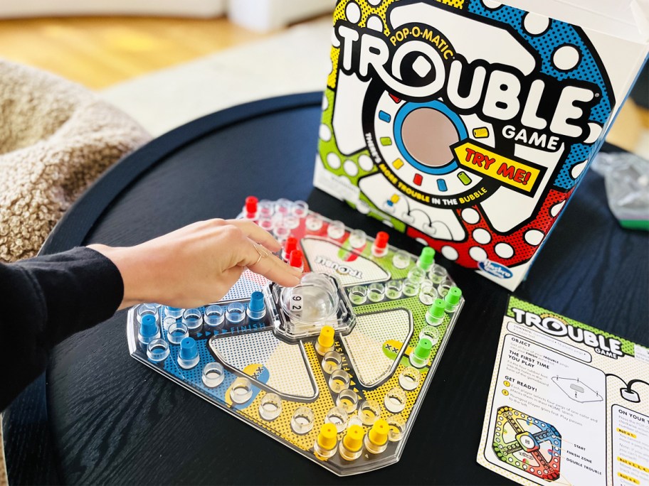 trouble board game for kids set up on black coffee table and hand pushing on bubble