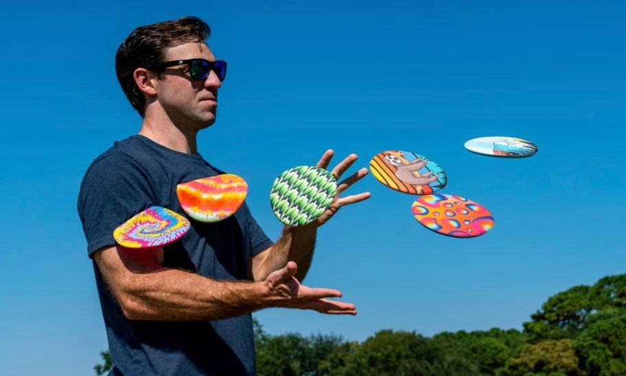 Man, standing with sunglasses and tons of flying silicone frisbees onlineing at him 