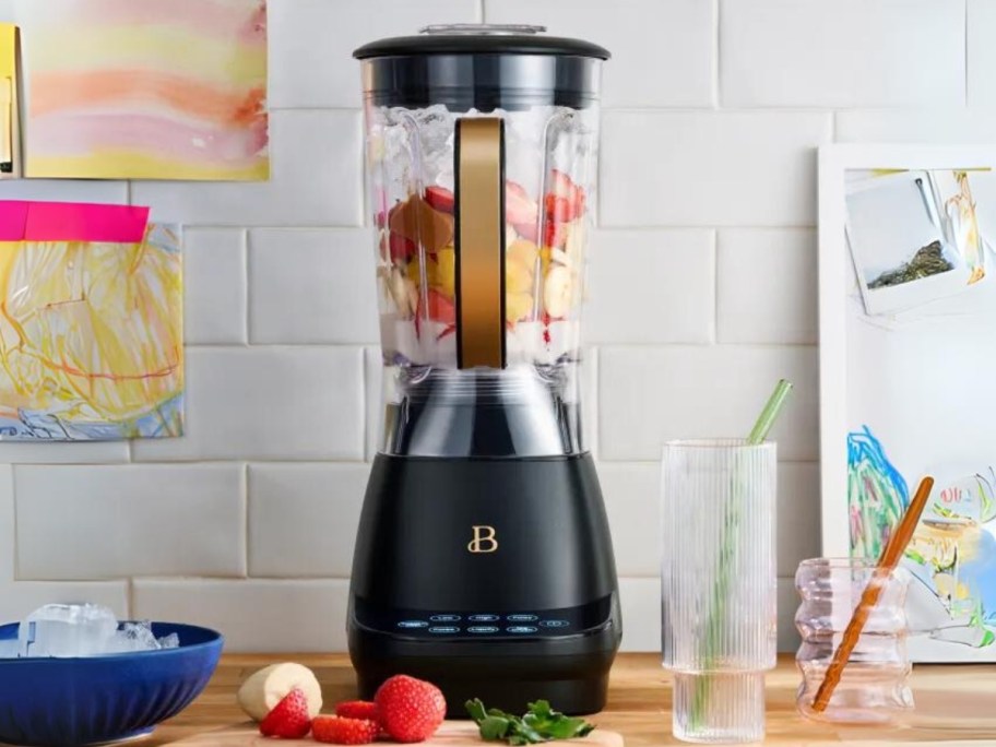 black and gold blender on counter with fruit in it and fruit laying around it