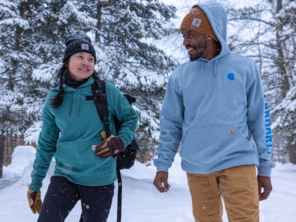 women wearing teal sweatshirt and man wearing blue sweatshirt walking in snow