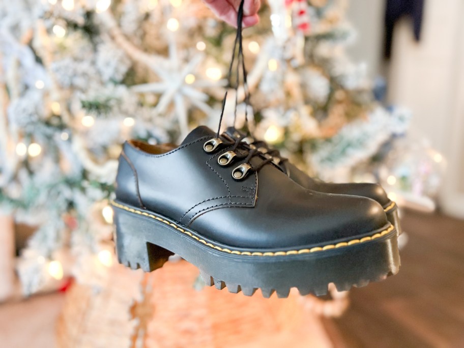 hand holding pair of black dr martens clogs