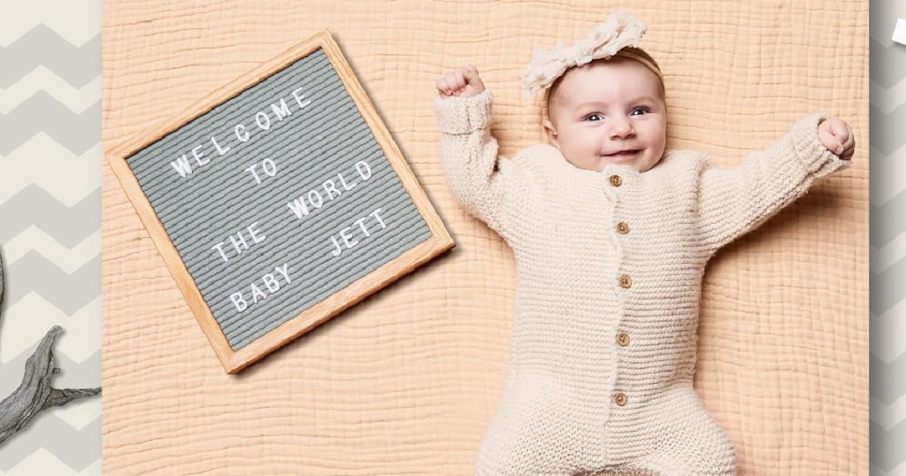 baby in a pink outfit on a pink blanket next to a felt letter board