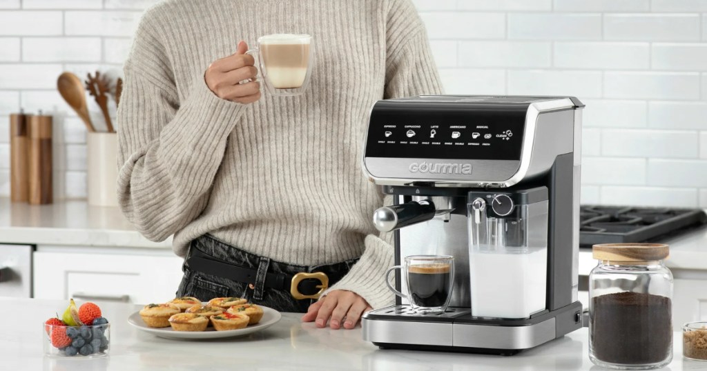 holding an espresso next to a home brew coffee machine