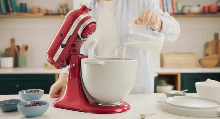 person pouring milk into bread bowl on red kitchenaid mixer