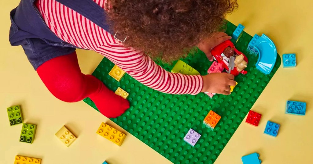 little girl putting legos on green baseplate