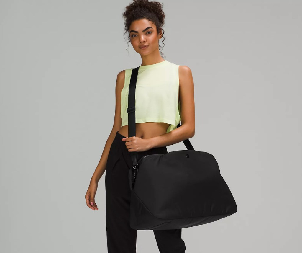 Stock photo of woman, holding large black Lululemon travel bag with gray background. 