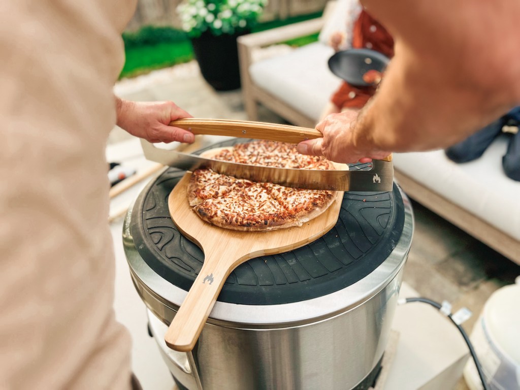 hands using rocker blade pizza cutter on top of silicone mat on solo stove