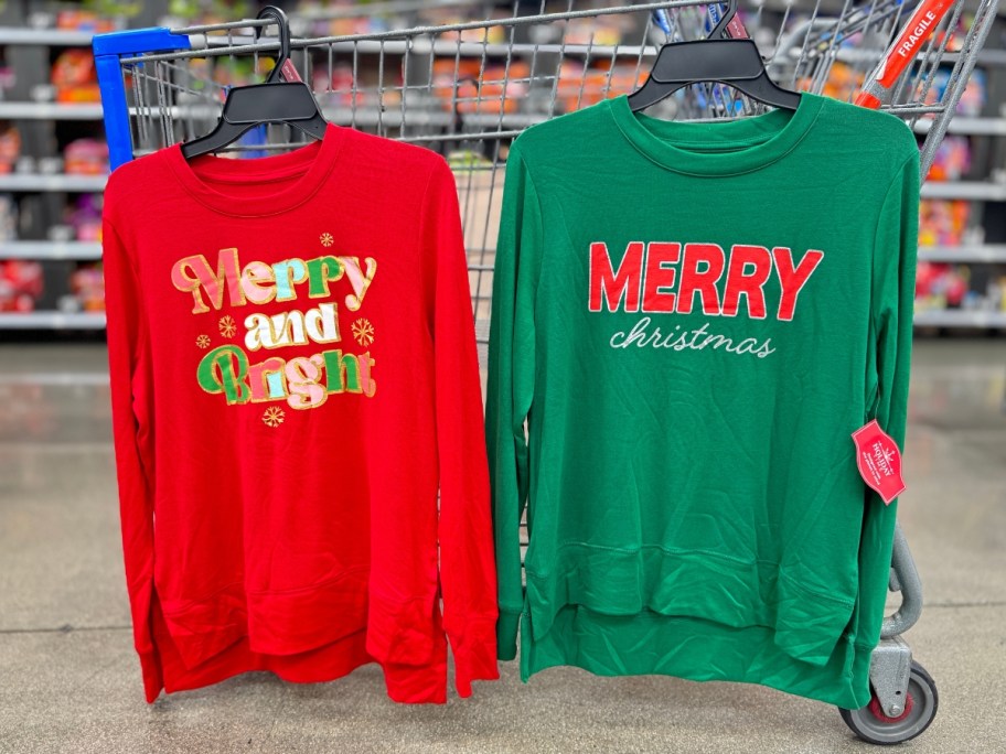 women's Christmas sweaters hanging on a Walmart cart - red with "Merry and Bright" and Green with "Merry Christmas"