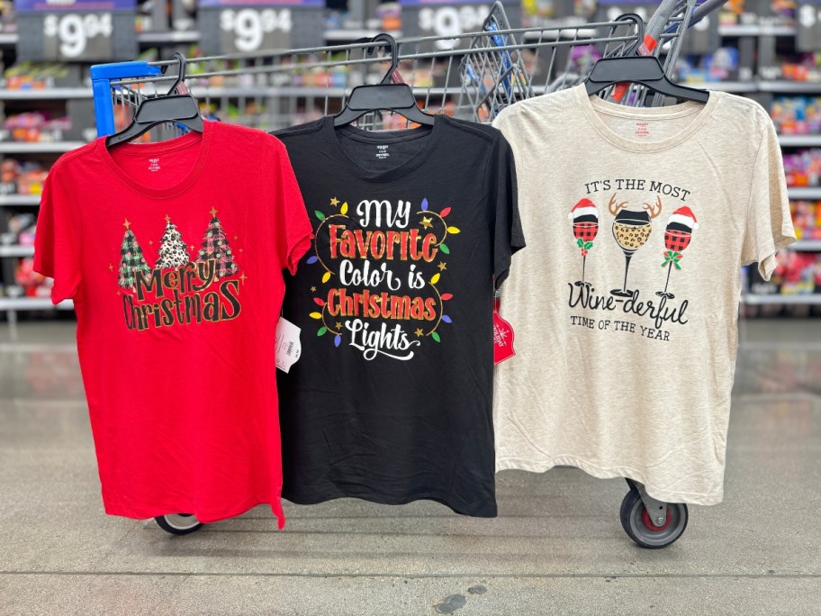 3 women's graphic Christmas tees hanging from a Walmart cart