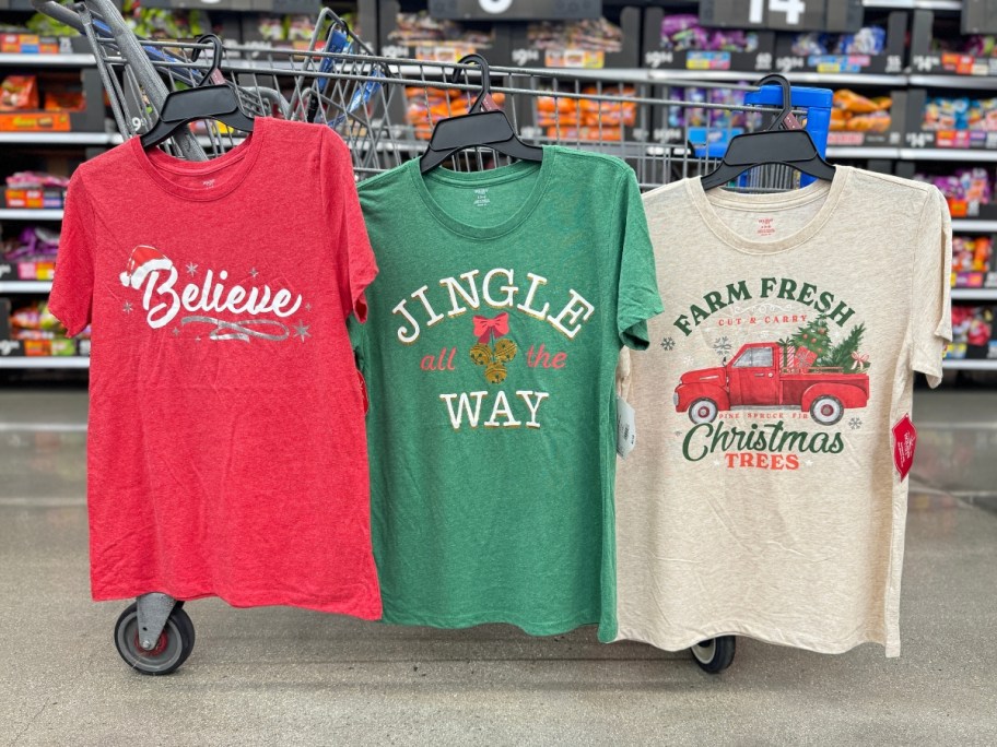 3 women's graphic Christmas tees hanging from a Walmart cart