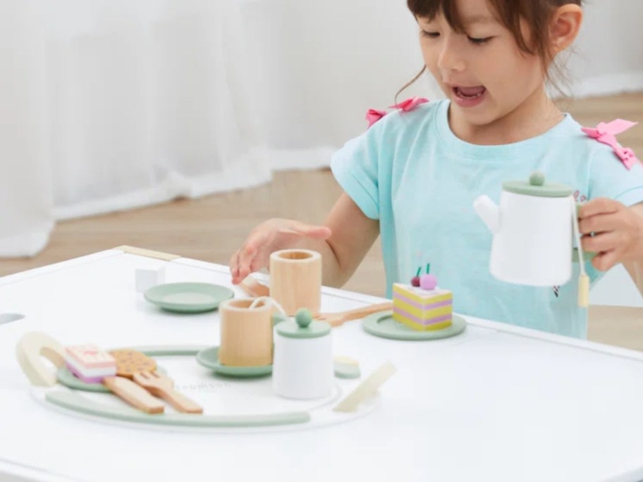 little girl playing with a wooden tea set