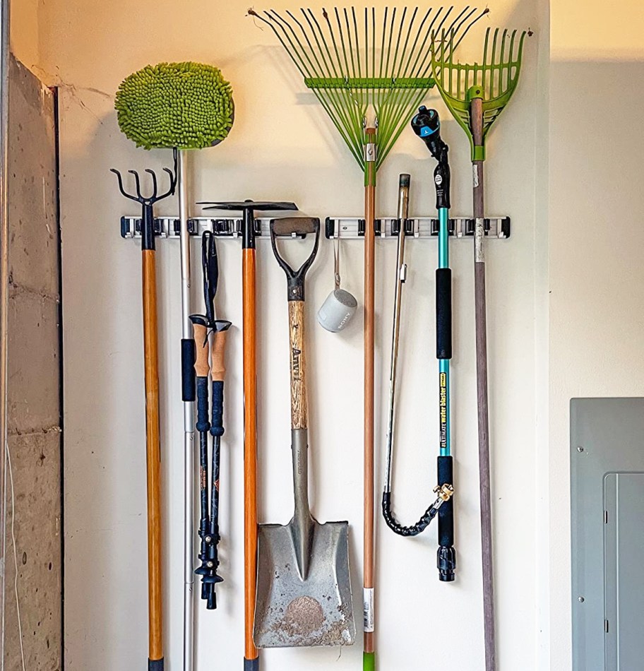 yard care items hanging on a wall-mounted broom holder in garage