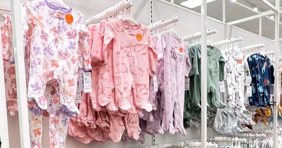 babies footed pajamas in a variety of colors and prints hanging on a wall display in Targer