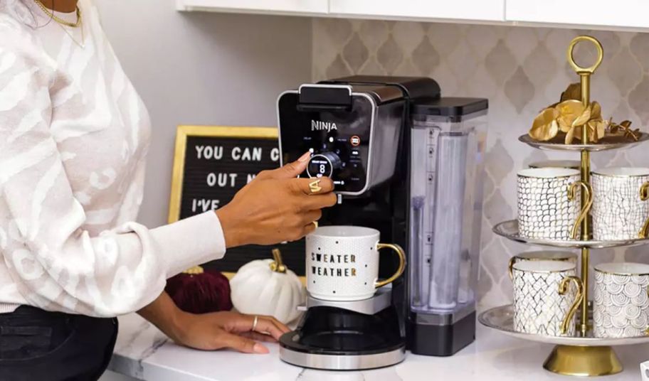 a woman brewing a cup of coffee in a kitchen with the Ninja DualBrew Pro Specialty Coffee System