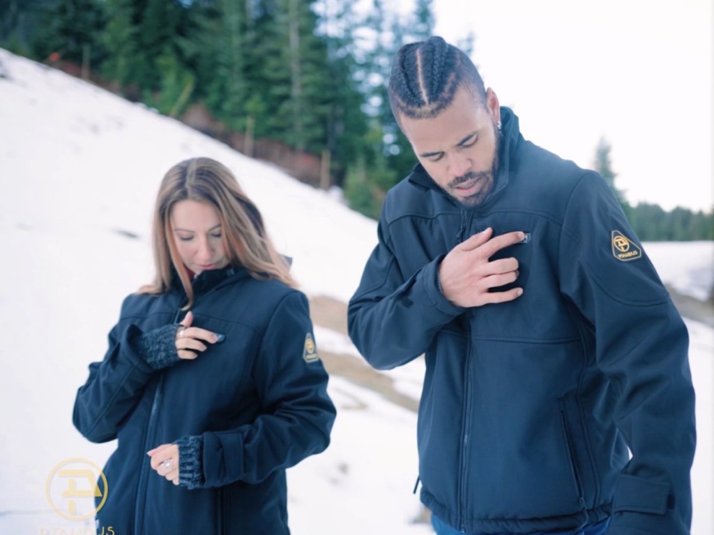 Man and woman walking outside in the snow, both wearing black heated jackets