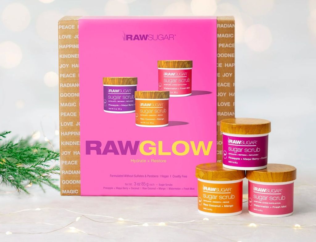 Raw sugar glow 3 piece gift set of scrubs next to a pine sprig 