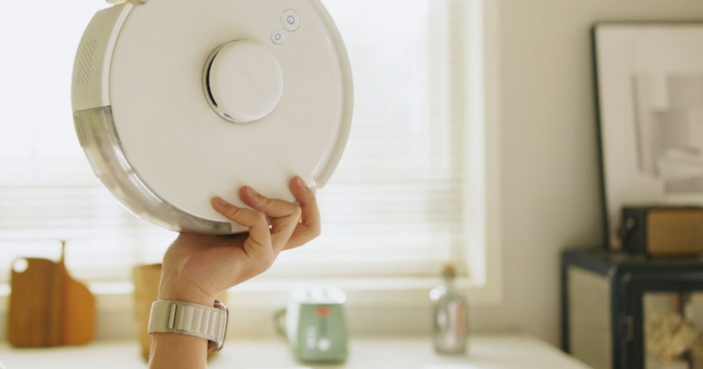 view of a woman's hand holding up a SwitchBot Robot Vac