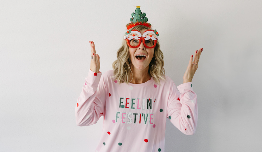 woman wearing pink polka dot feeling festive pajamas with santa glasses and tree headband