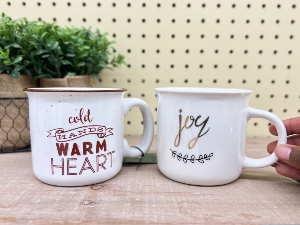 hand holding two ceramic holiday mugs