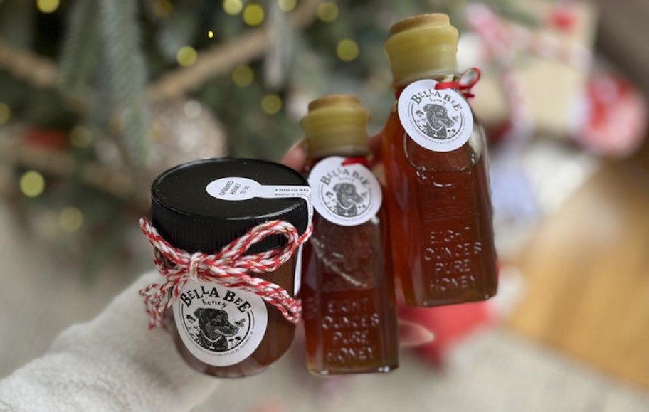 arm holding 3 jars of honey in front of christmas tree 