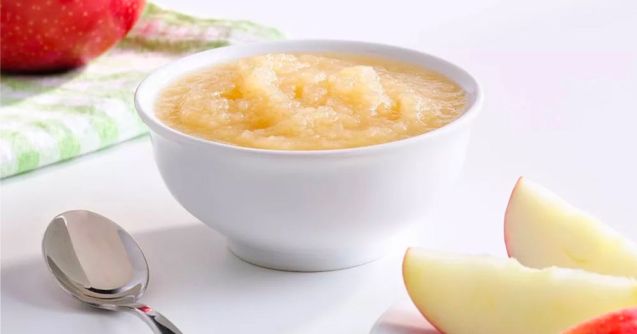 mott's applesauce in white bowl on table next to spoon and apple slice