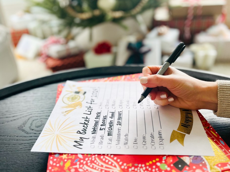 someone filling out a new years bucket list with a christmas tree in the background