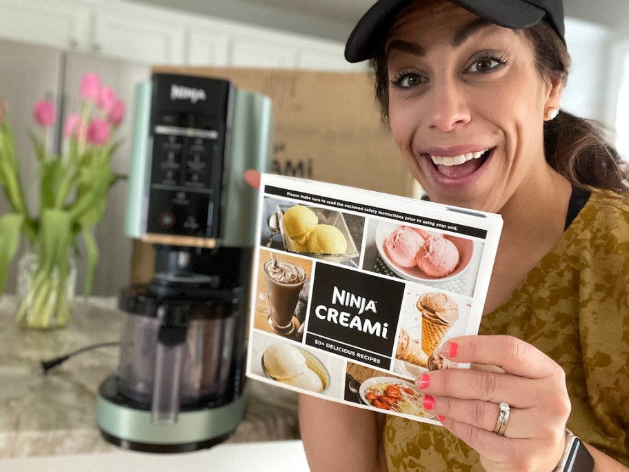 woman holding up the ninja creami recipe book next to her ninja creami ice cream maker machine