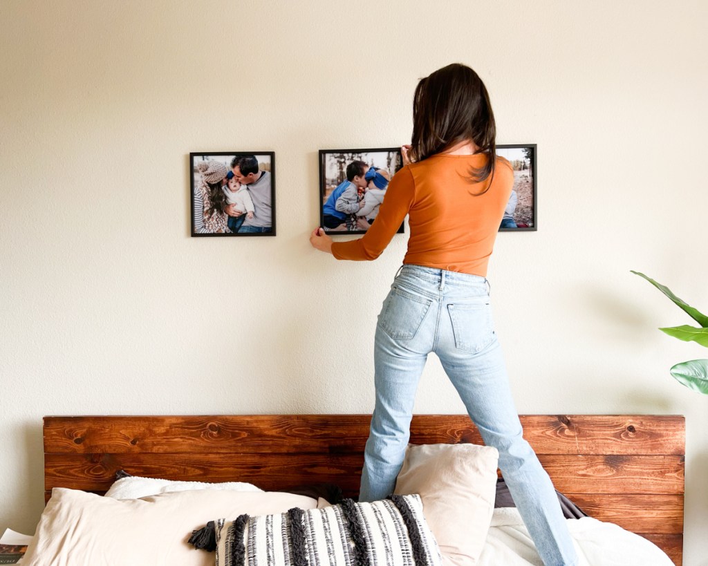 woman standing on bed hanging black tilepix frames on walls