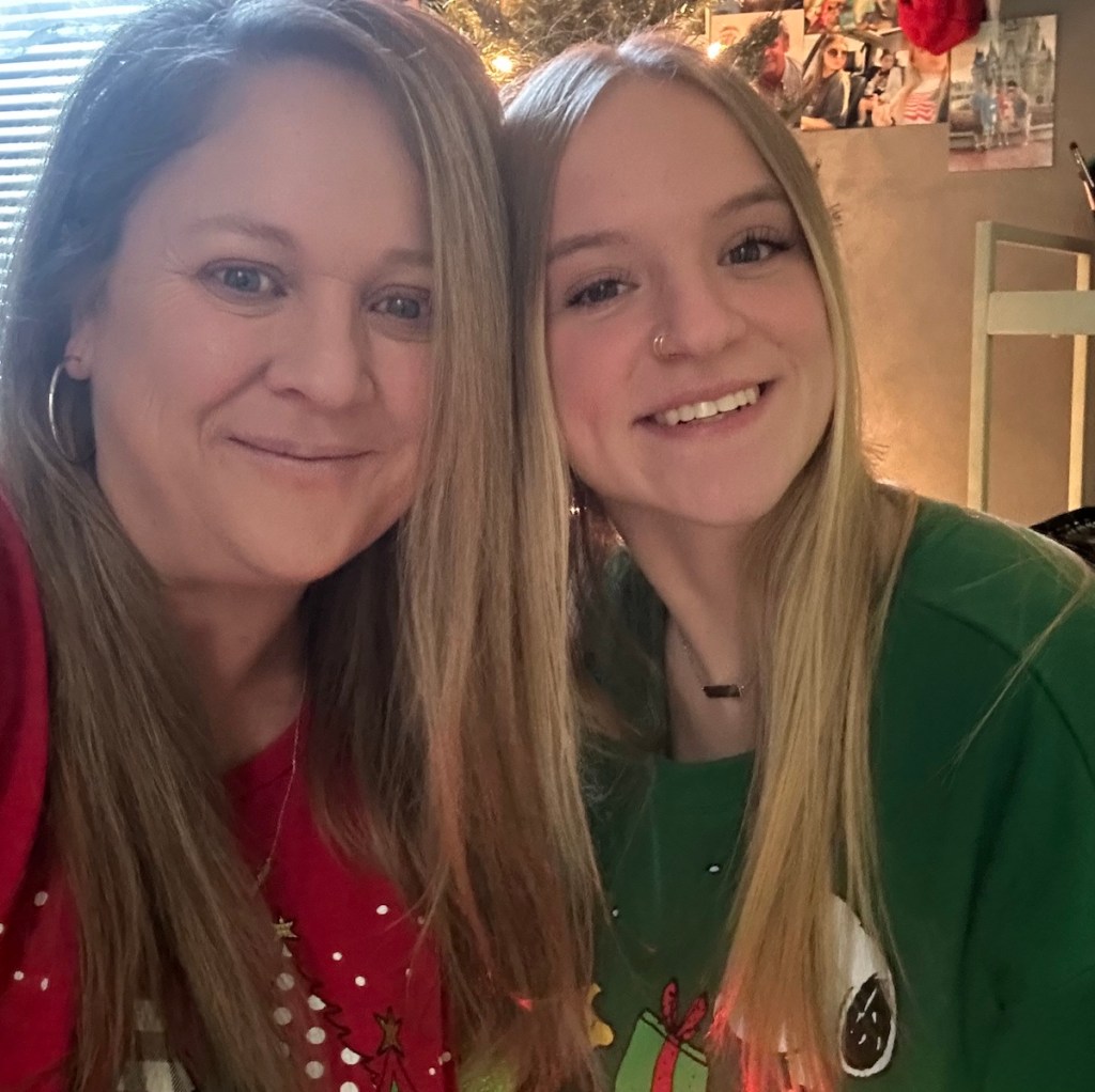 woman and teen girl taking selfie in front of wall with christmas lights