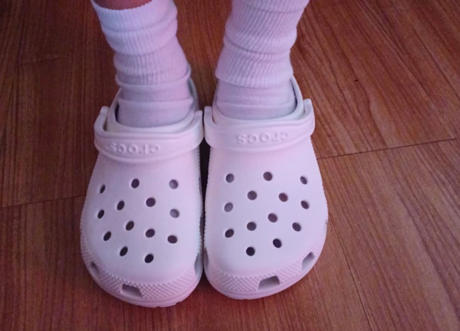 close up of kid wearing white crocs with white high socks standing on wood floor