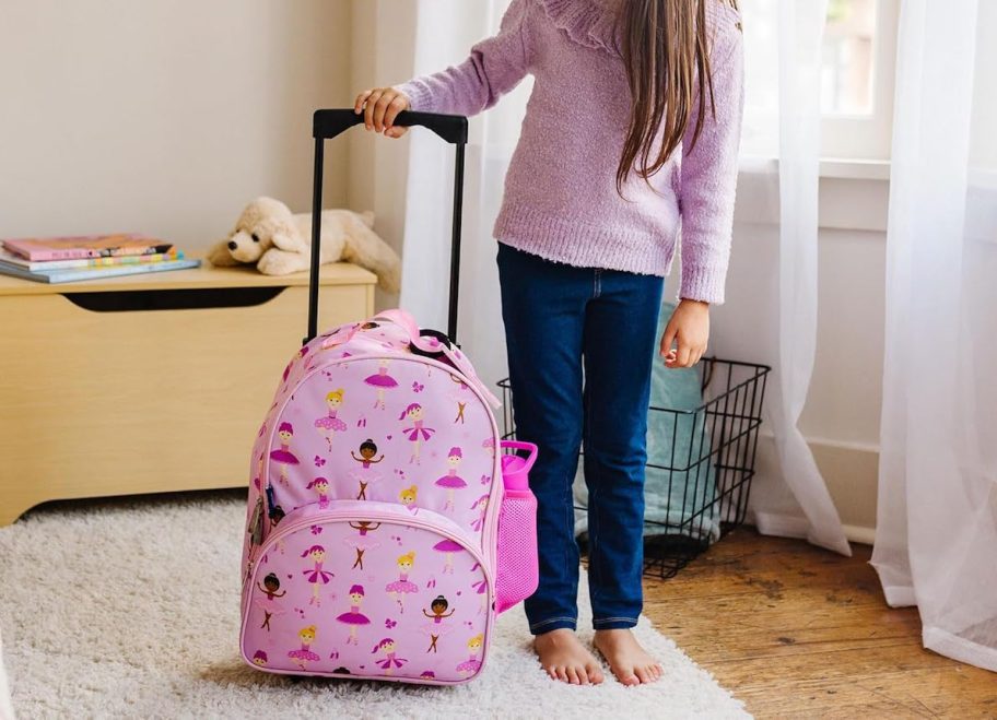 girl holding handle on backpack roller in room with toy box