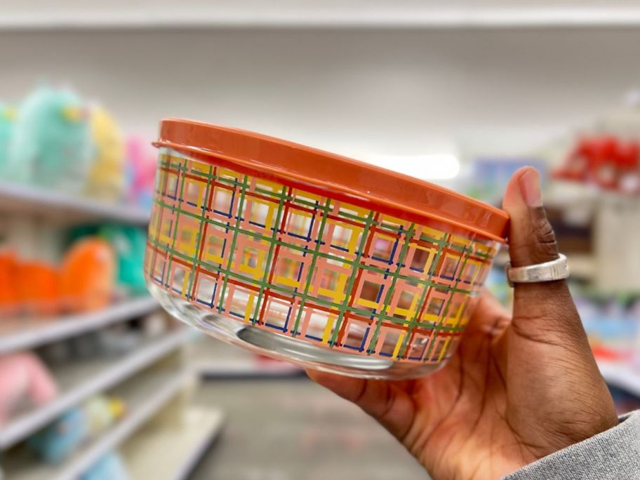 hand holding a glass food container with a plaid design on it and a peach/orange lid